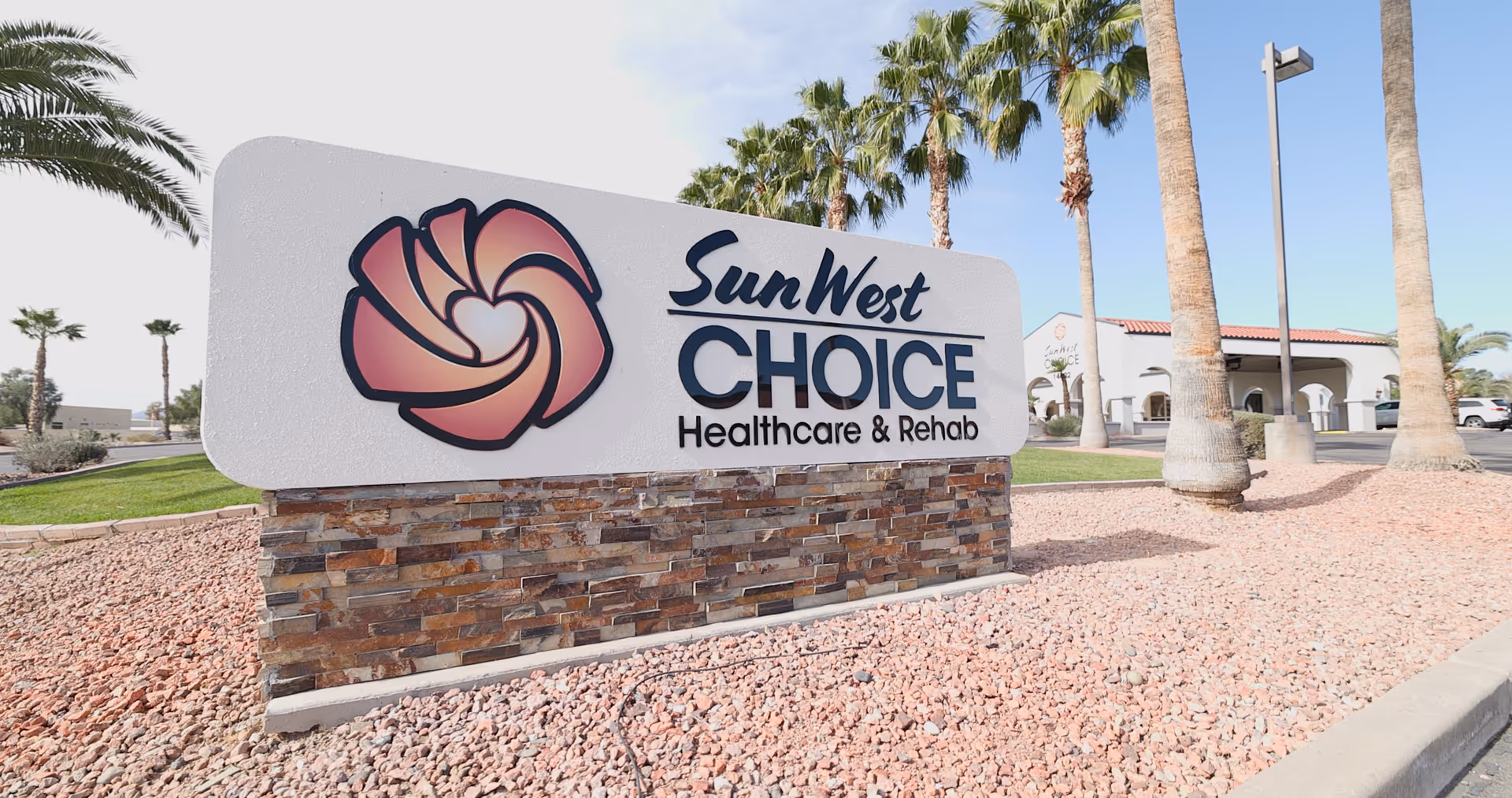 Sun West Choice Healthcare & Rehab sign on a stone pedestal at facility entrance.