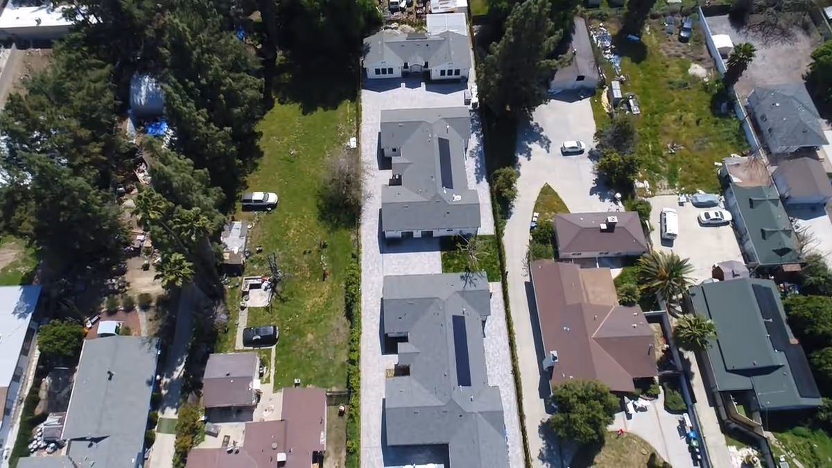 Aerial view of a residential street with several buildings and green spaces.