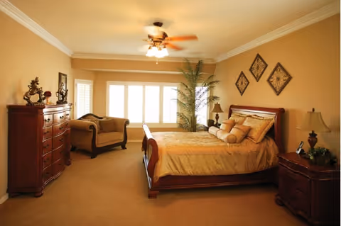Spacious bedroom with a large bed, dresser, sofa, and warm beige decor.