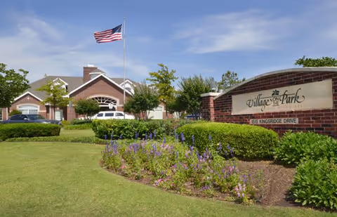 Front exterior of Village on the Park Oklahoma City with sign, flag, and landscaping