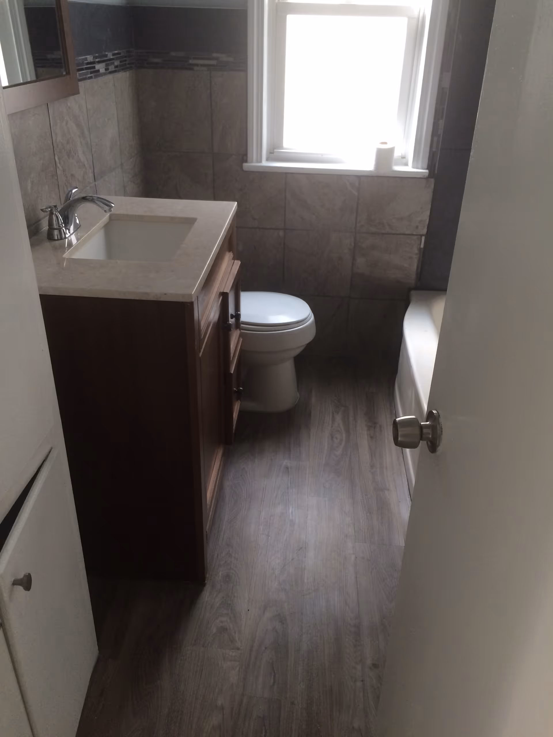 Small bathroom with a vanity, toilet, tub, and tiled walls.