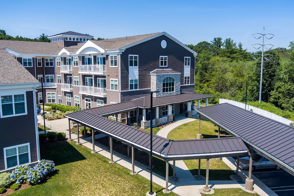 A modern senior living facility exterior with a long covered walkway and manicured lawn.