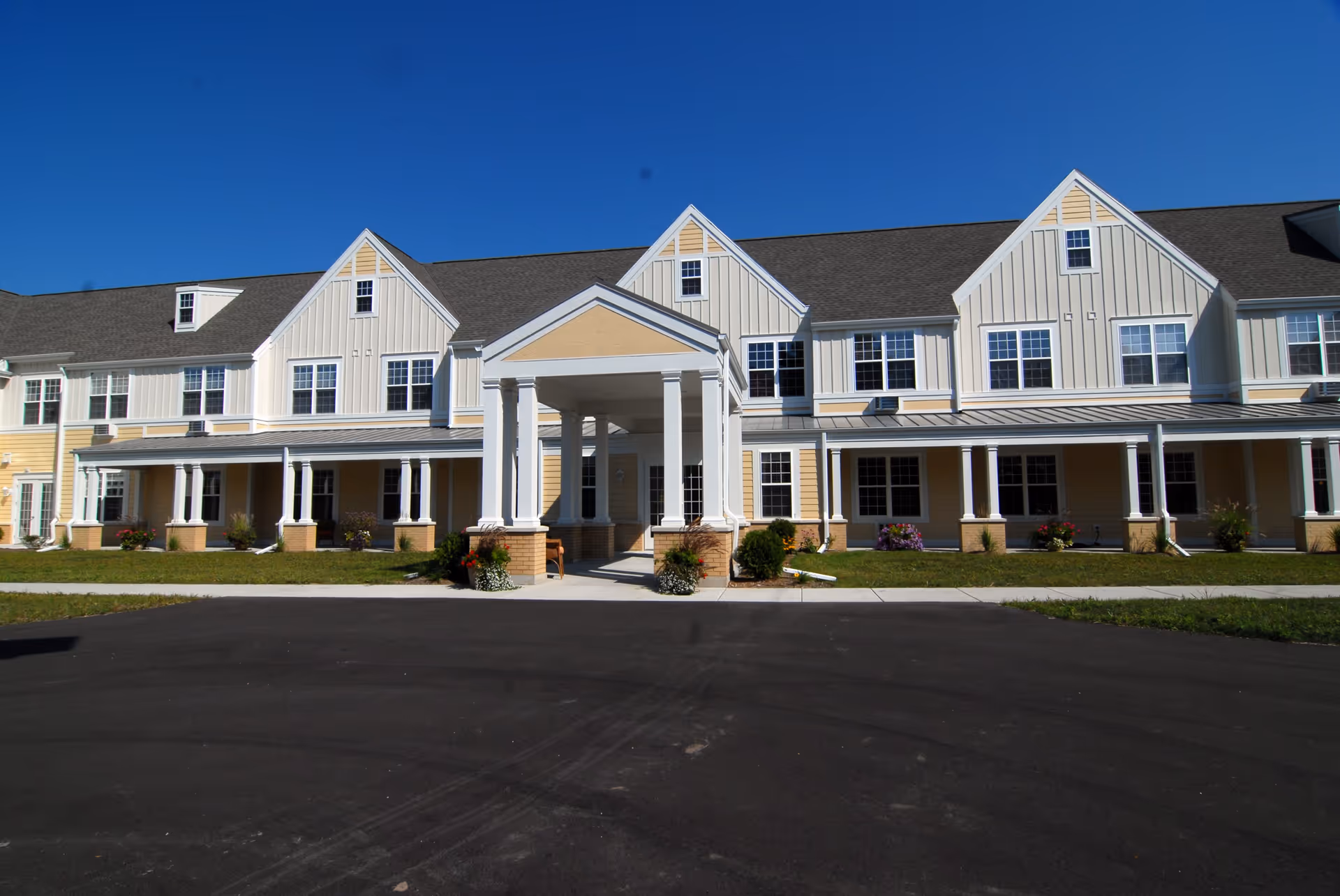 Front view of a two-story yellow-and-white building with a covered columned entrance under a clear blue sky.