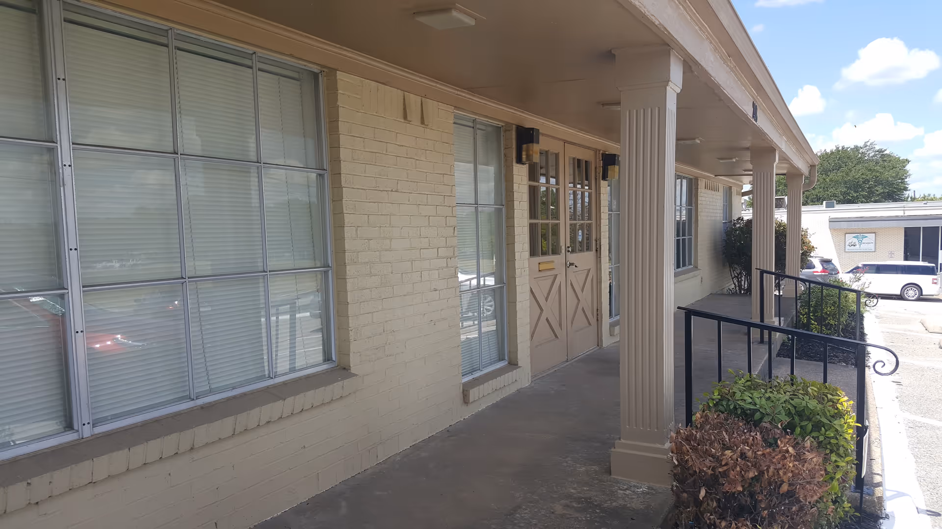 Exterior view of a beige brick senior facility entrance with a porch and large windows.