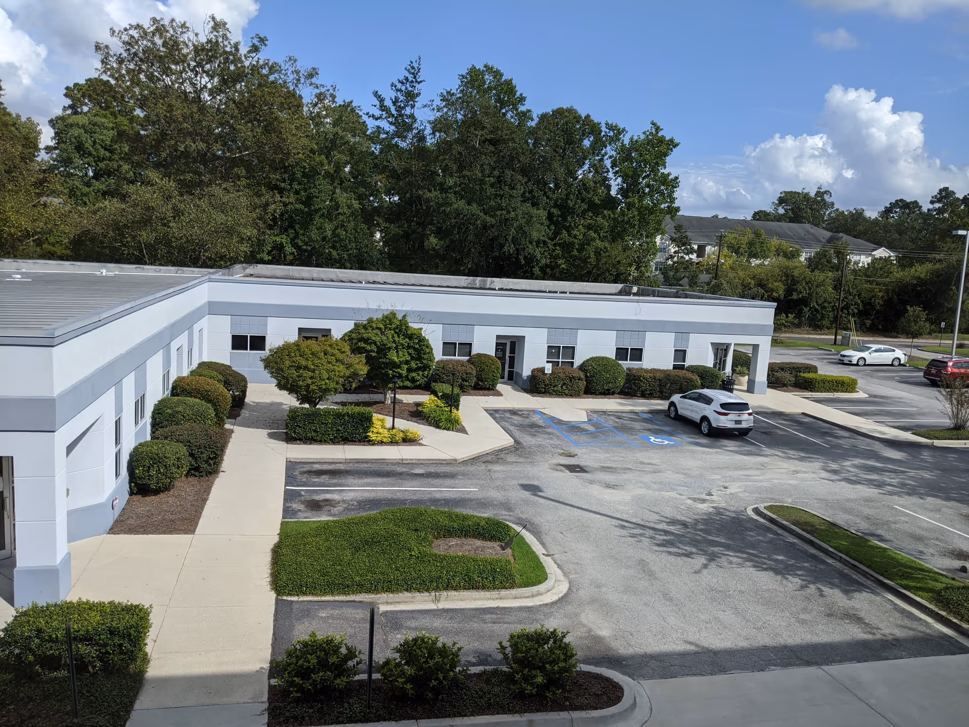 A single-story light-blue facility with parking lot, landscaped shrubs, and trees in front.