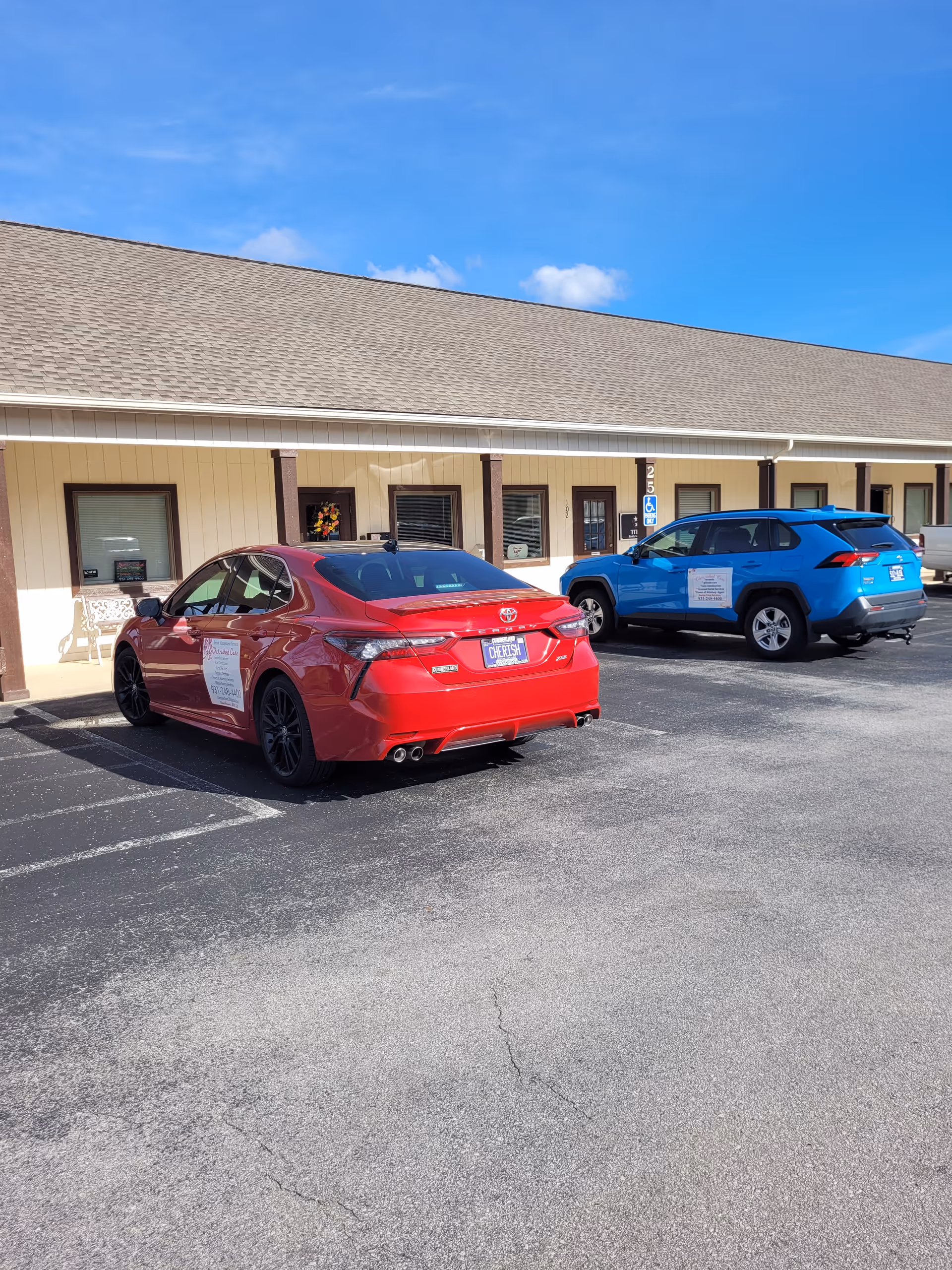 Two cars parked in front of a beige senior care facility under a blue sky.