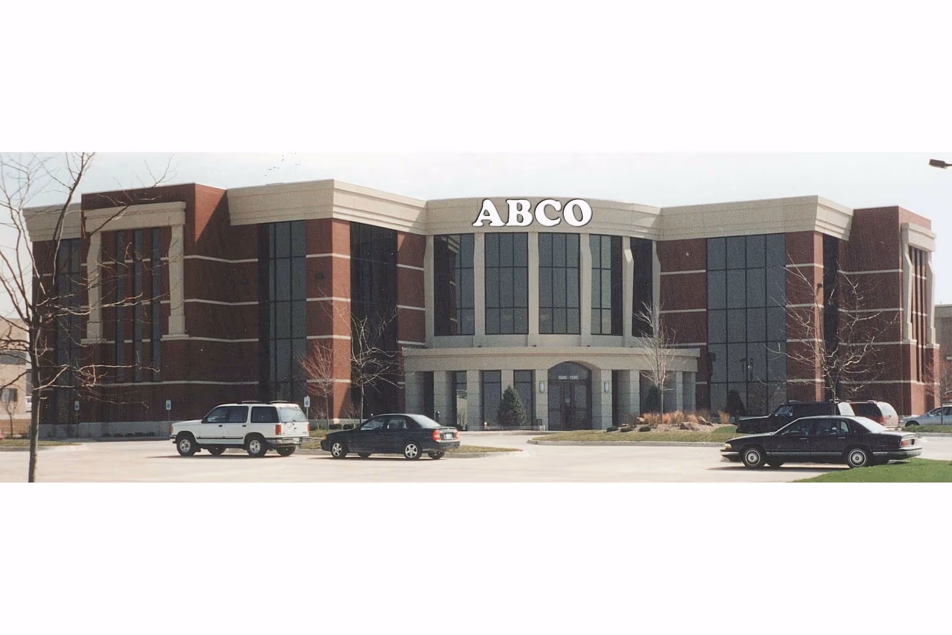 Exterior view of a large brick building with glass windows and parked cars in front.