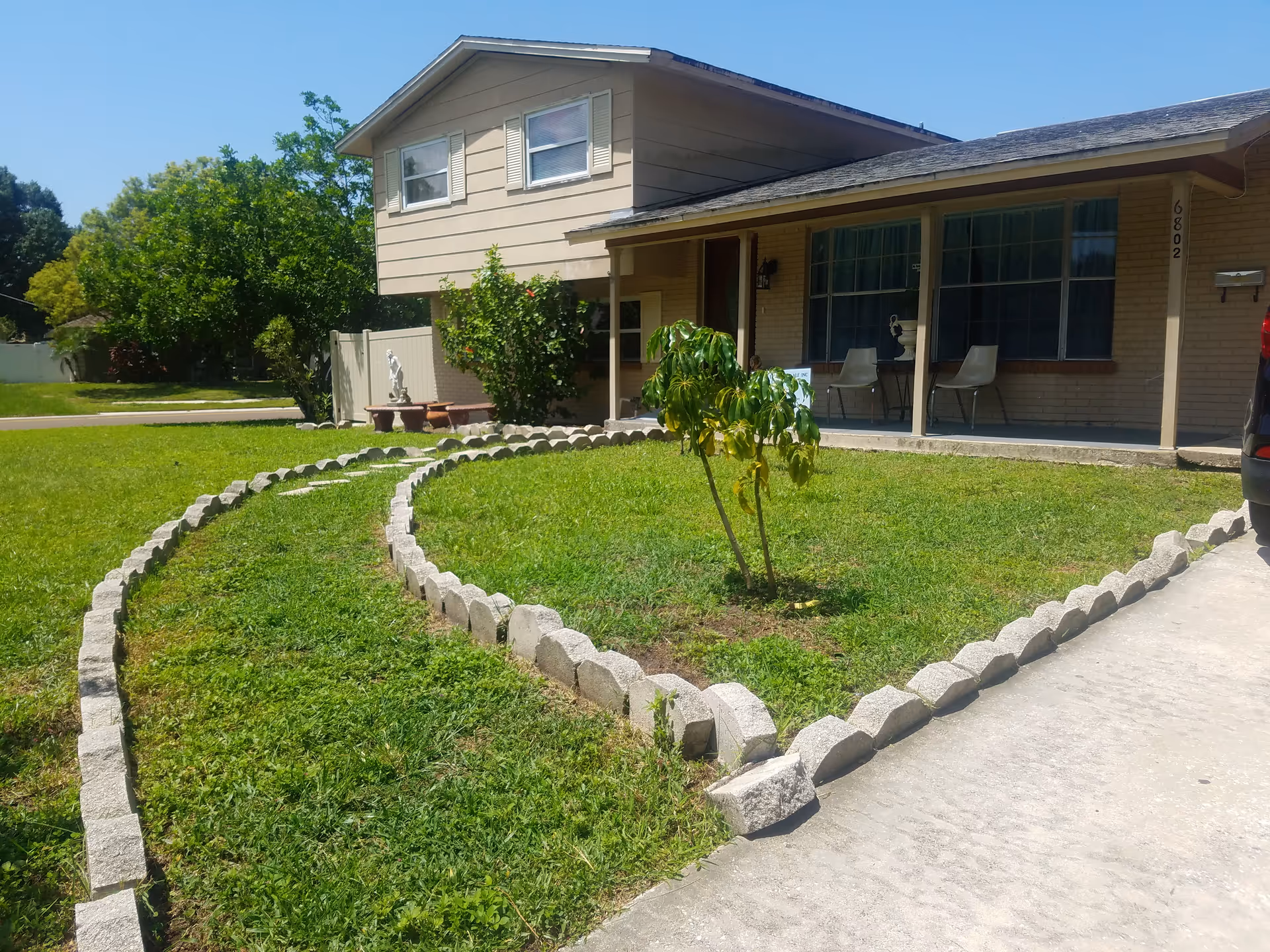 A single-story beige senior living facility with a landscaped front yard and porch seating.
