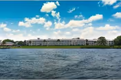 A long retirement living building sits along a calm river under a blue sky.