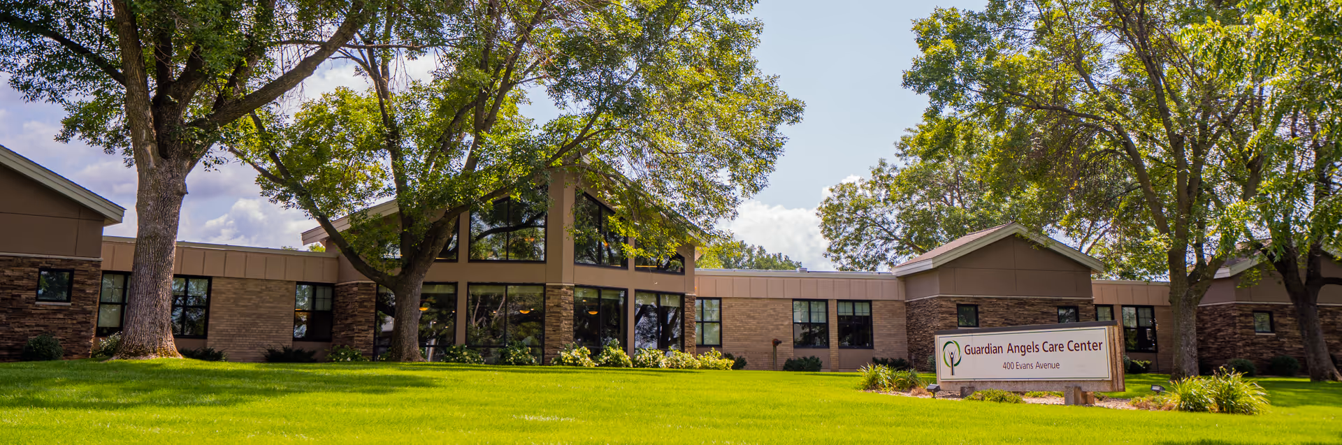 Front view of Guardian Angels Care Center building with trees, lawn, and sign in foreground.