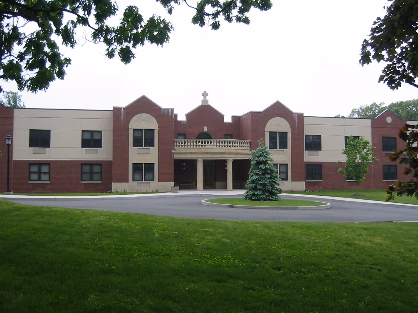 Front view of a two-story brick and beige senior living building with a covered entrance, circular driveway, and lawn.