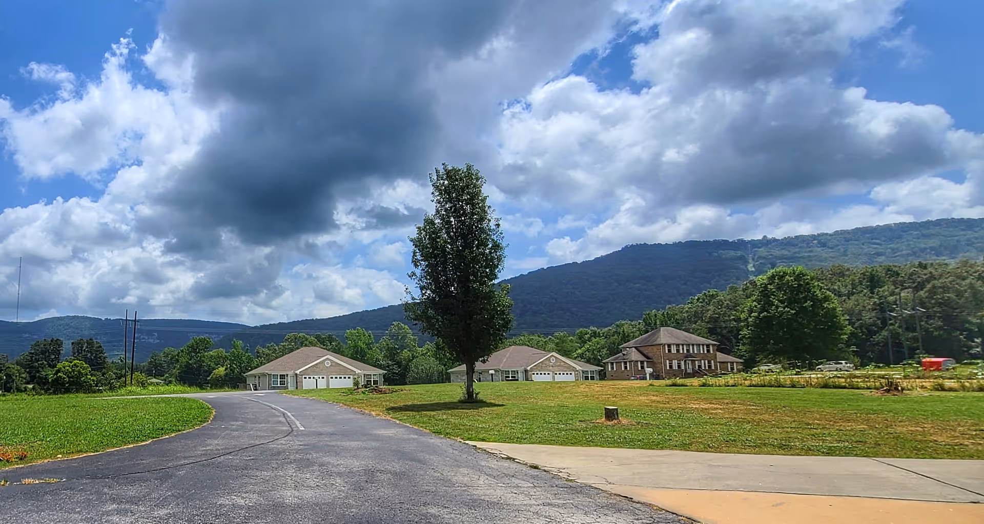 Exterior view of a rural senior living campus with multiple houses, a tree, and distant hills.