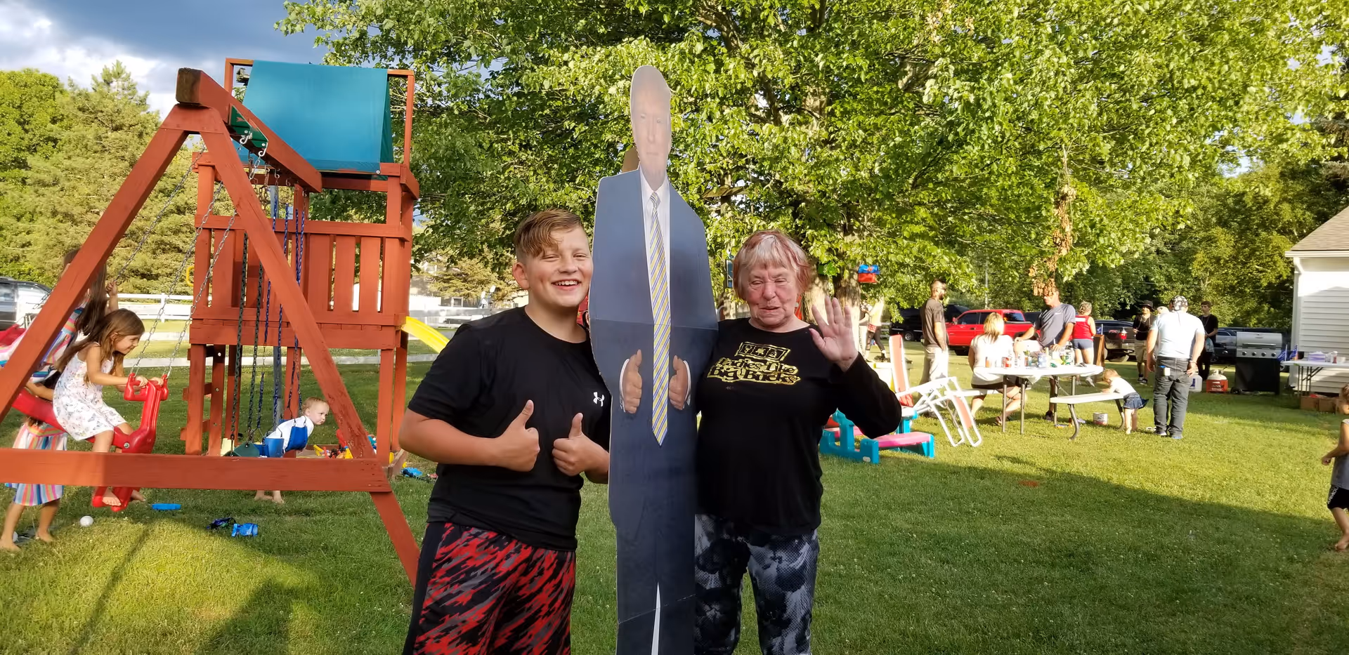 Two people pose beside a cutout of a man in a suit outdoors near a playground.