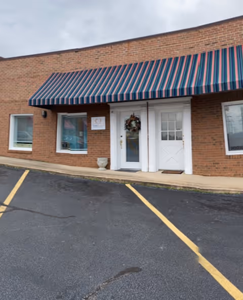 Brick building entrance with striped awning, wreath, and white doors.