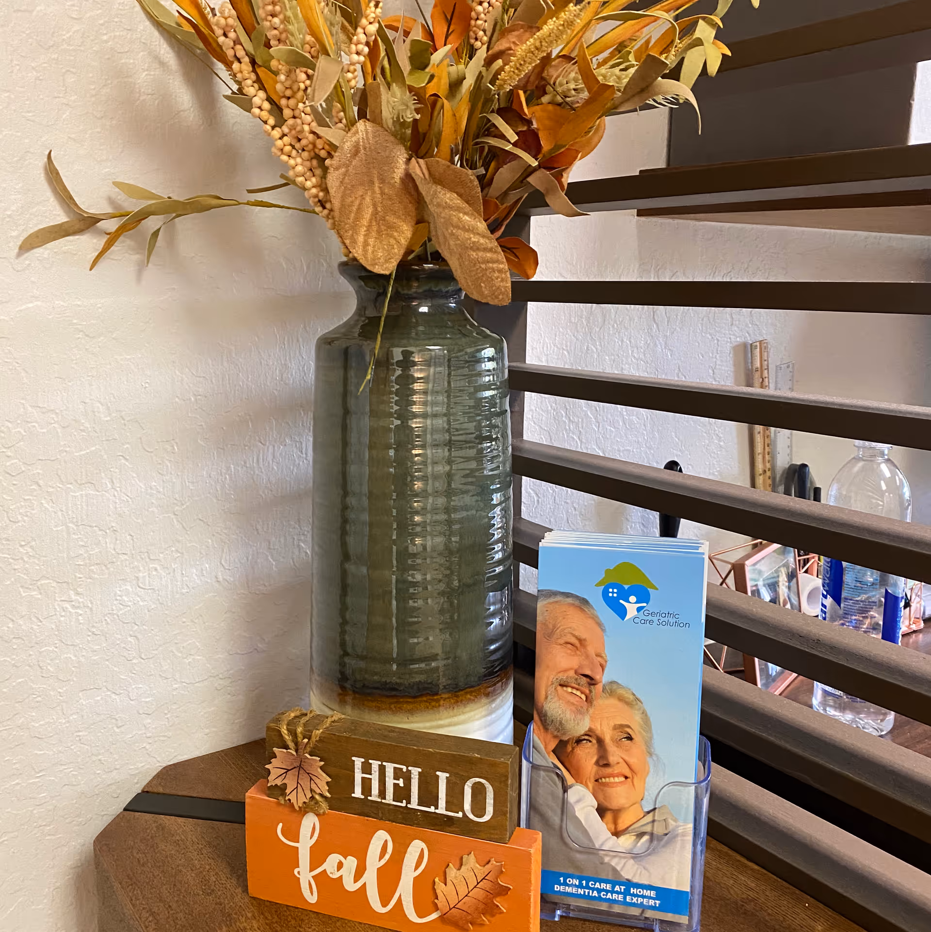 Tall vase with dried floral arrangement beside staircase in a geriatric care facility lobby.