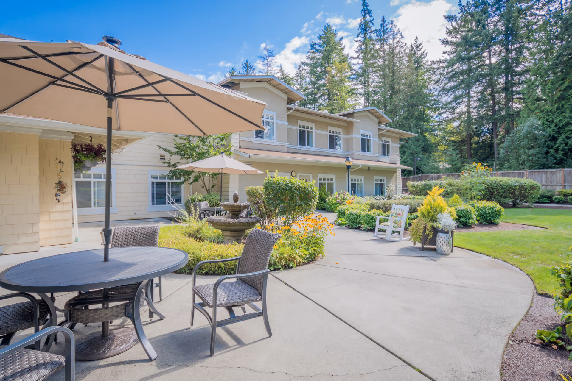 Sunny outdoor patio with tables, chairs, umbrellas beside a senior living building.