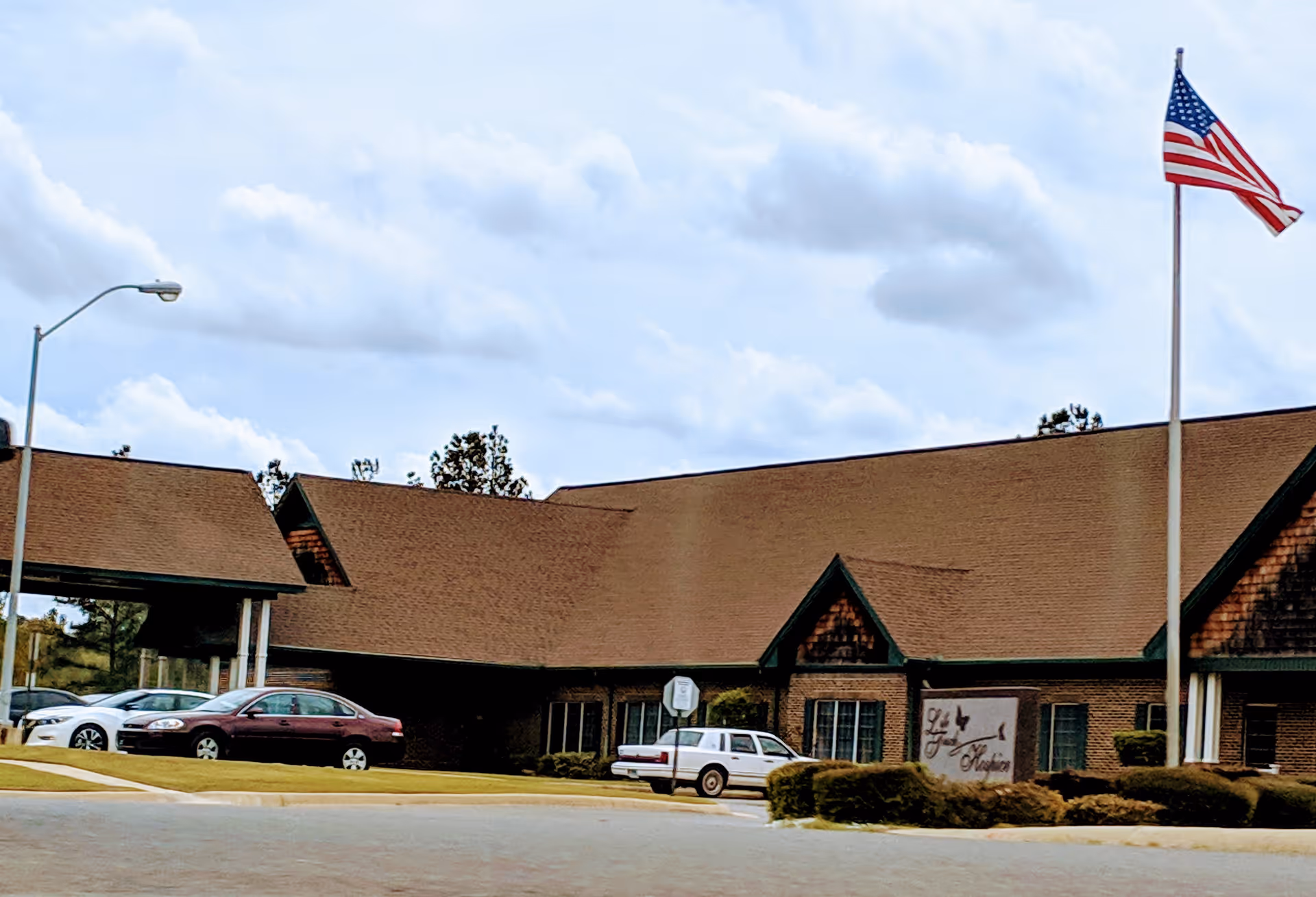 Front view of Life Touch Hospice building with flag and parked cars outside.