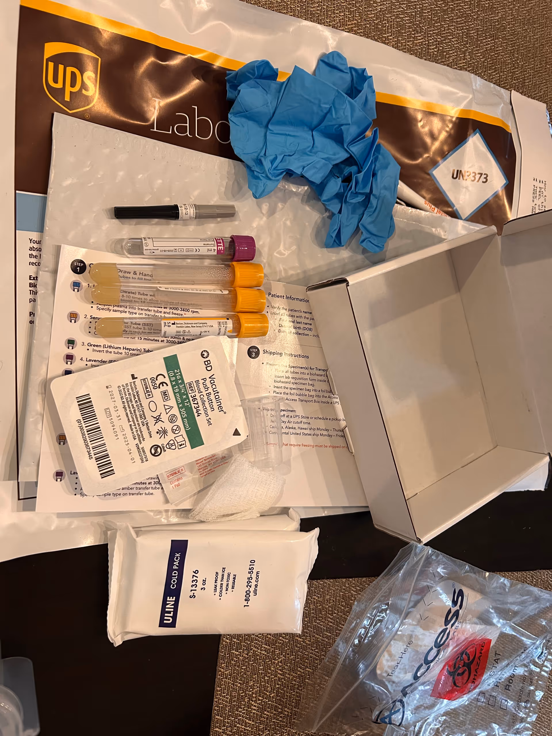 Open box with medical supplies, test tubes, and blue disposable gloves on a desk.