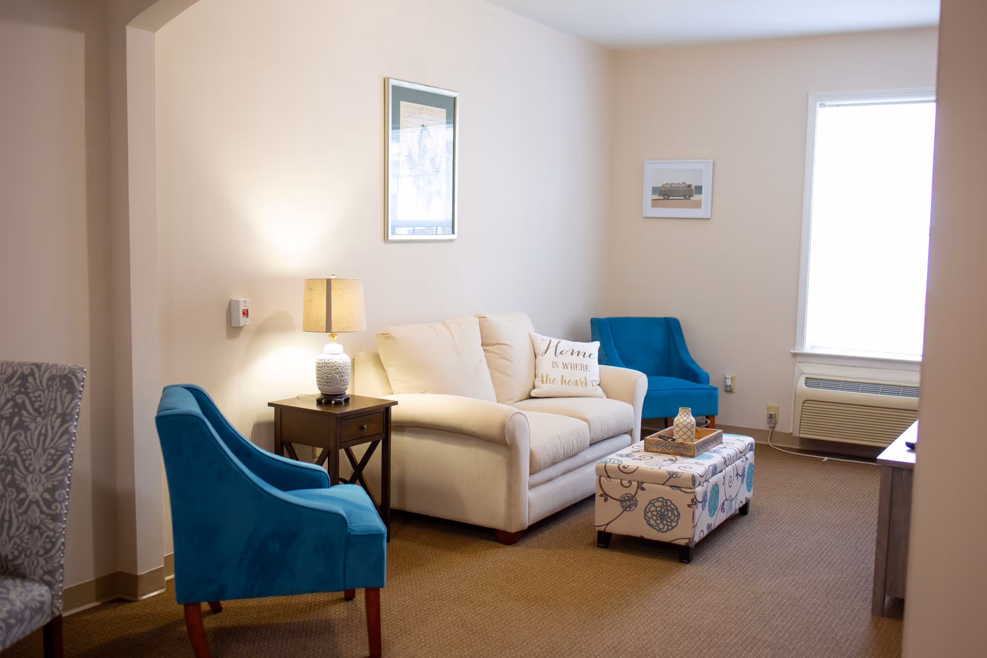 Cozy living room in a senior living facility with beige sofa, blue chairs, ottoman.