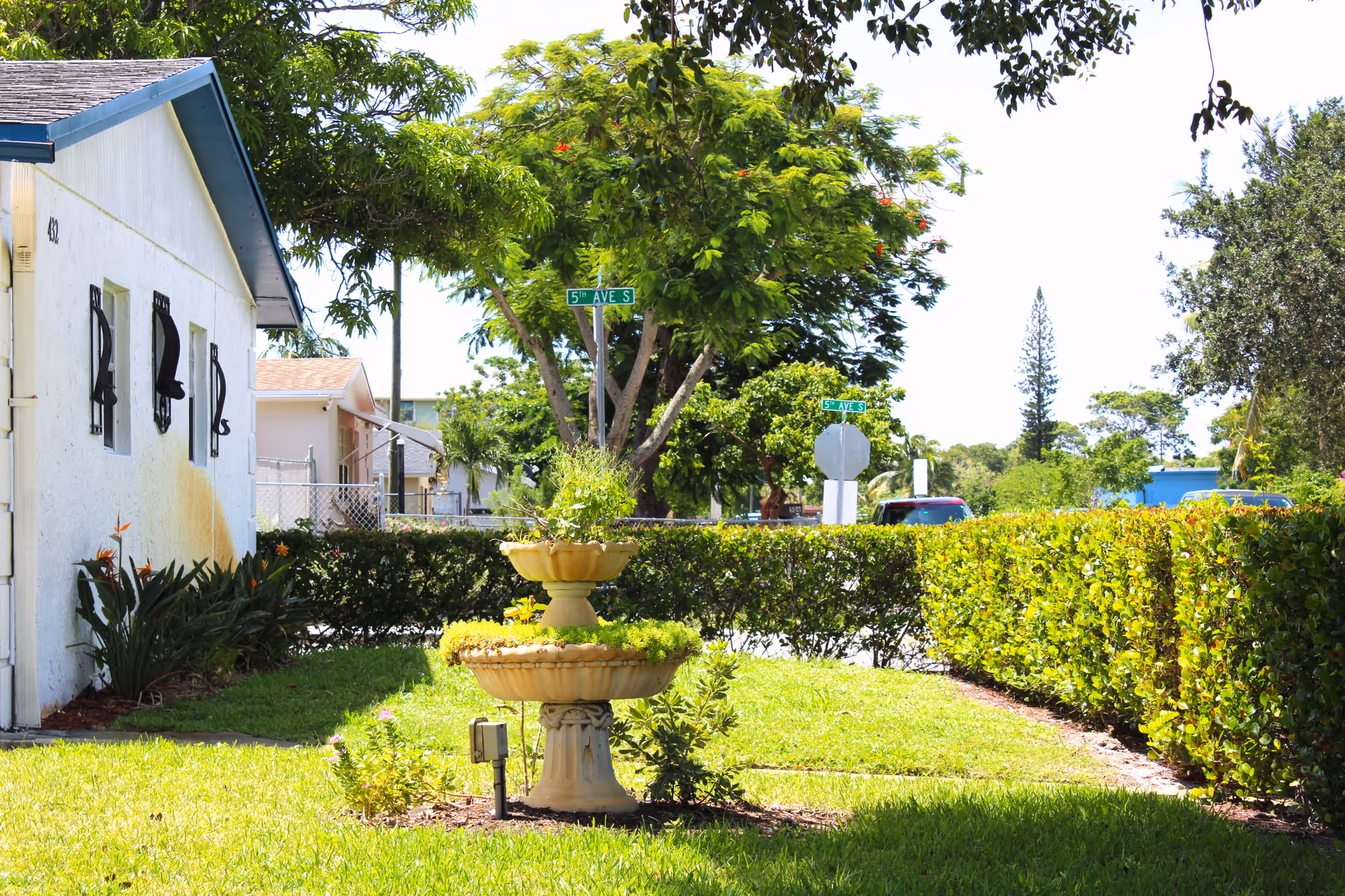 Exterior of a senior living facility with a decorative fountain, hedges, and trees.