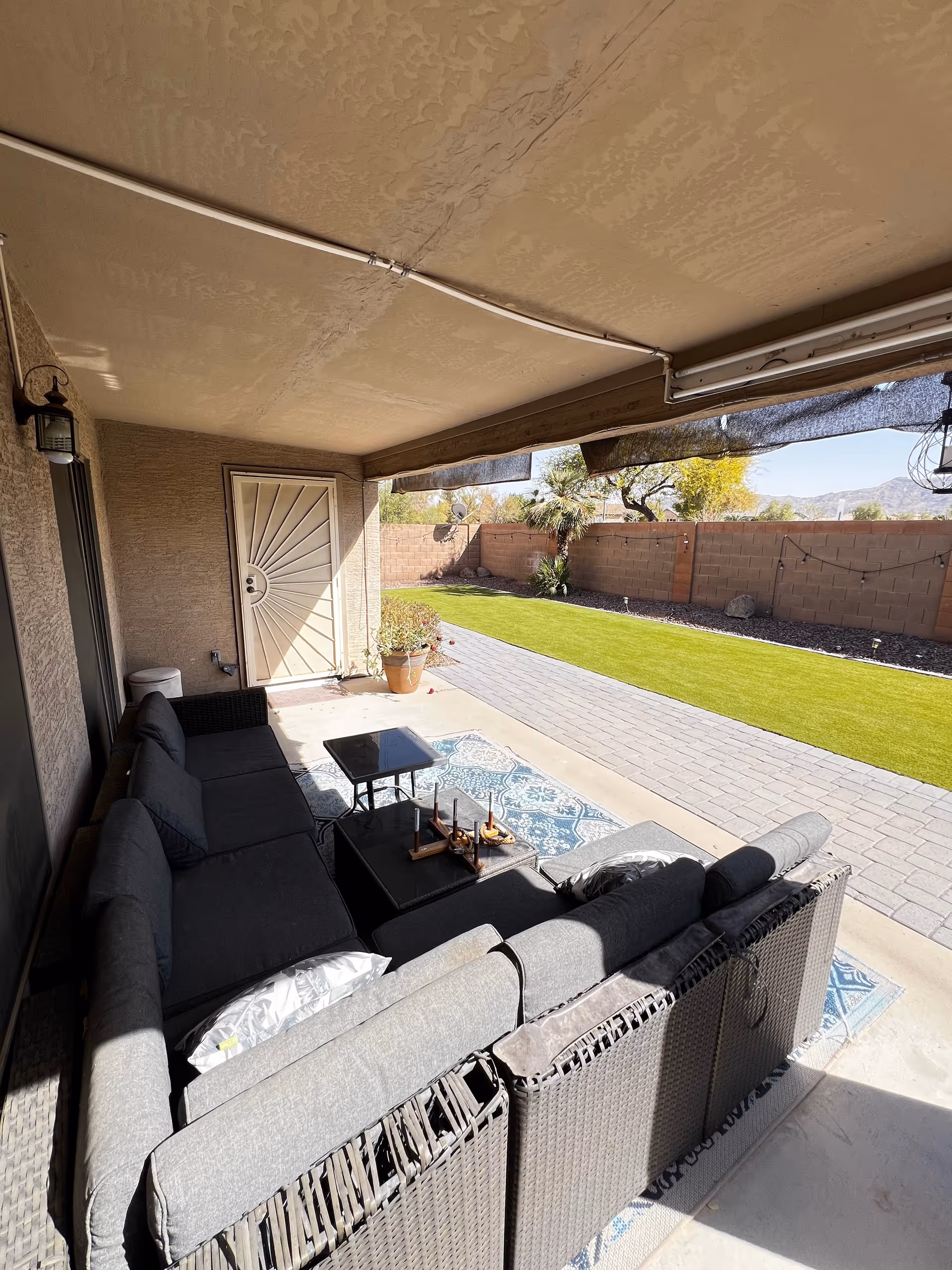 Covered outdoor patio with gray sectional seating, coffee table, and grassy yard.