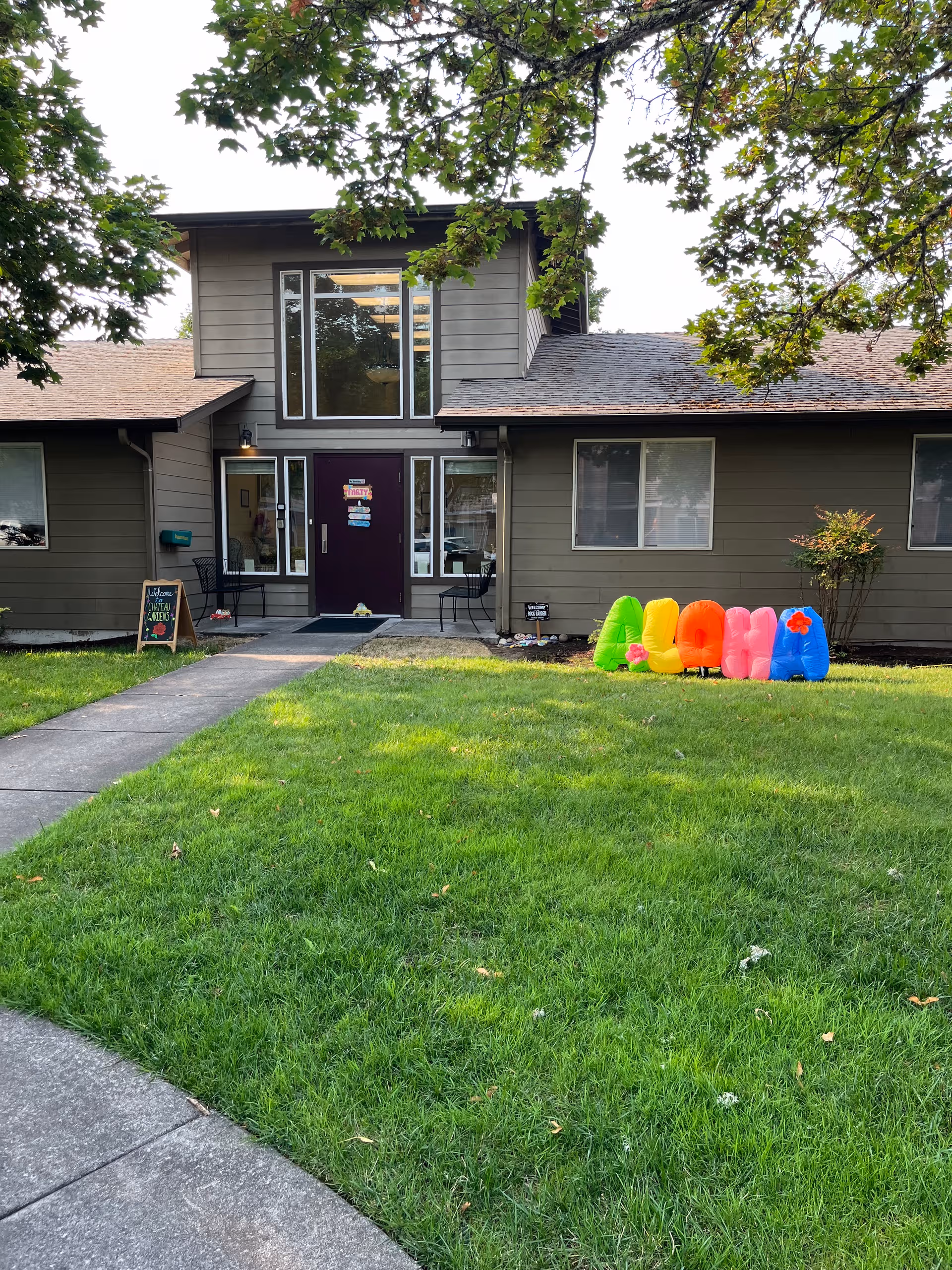 Front view of Chateau Gardens Memory Care building with grassy lawn and colorful chairs.