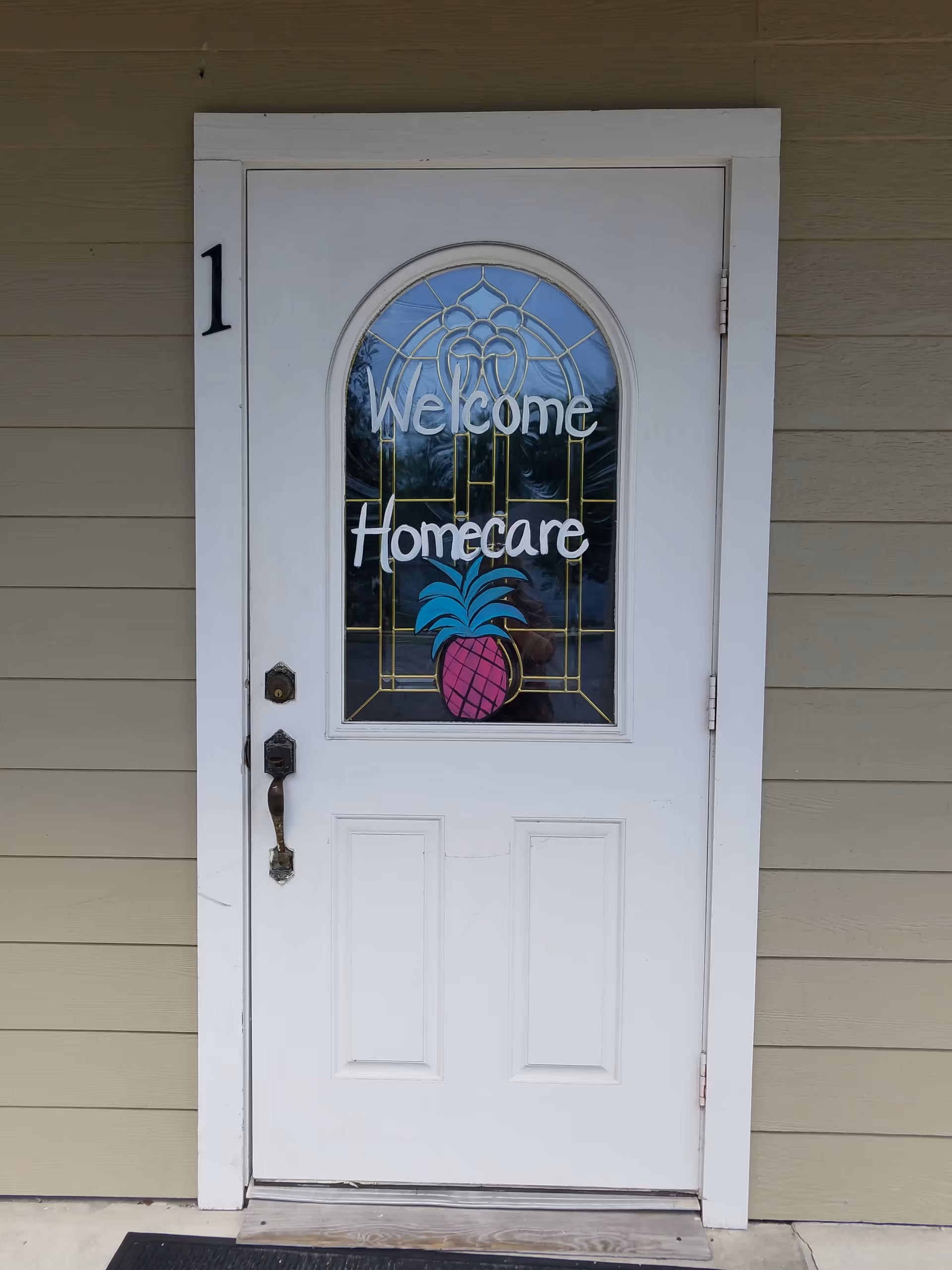 White exterior door with a stained glass window reading Welcome Homecare and a pink pineapple graphic.