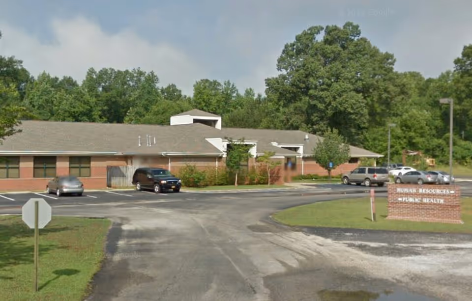 Exterior view of a single-story brick health department building with a parking lot.