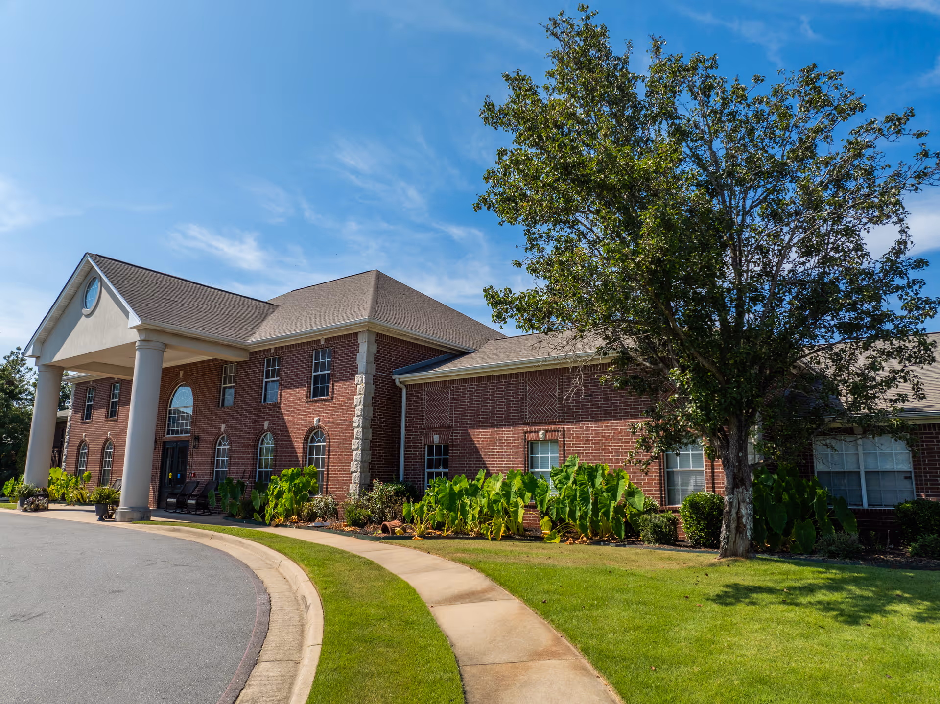 Brick senior living facility with arched windows, columns, and a curved driveway.