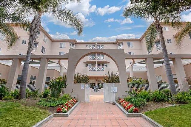 Exterior view of Brookdale Santa Monica Gardens showing the arch entrance, palm trees, and landscaped path