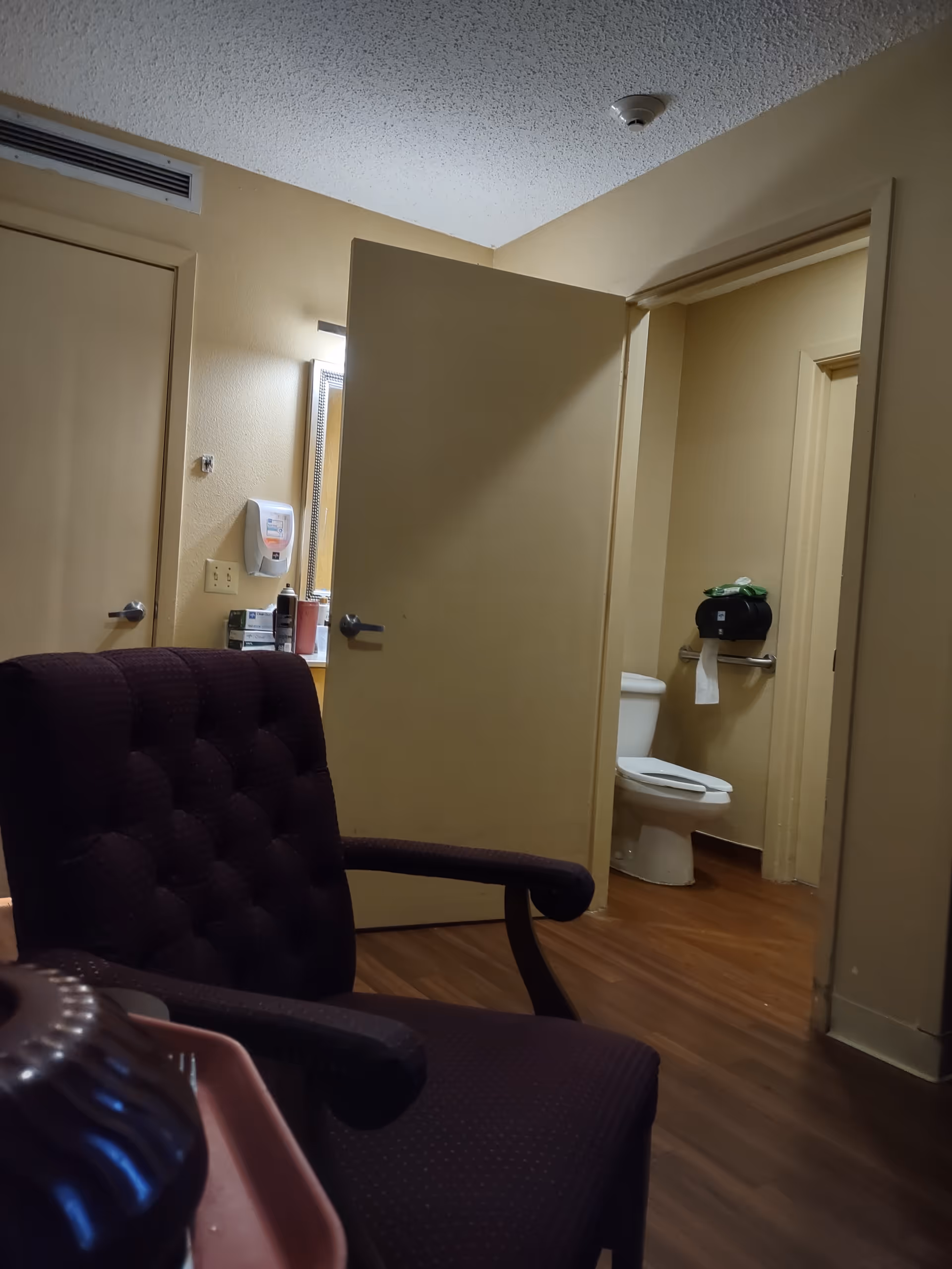 Interior view of a lounge with a purple chair and open bathroom door.