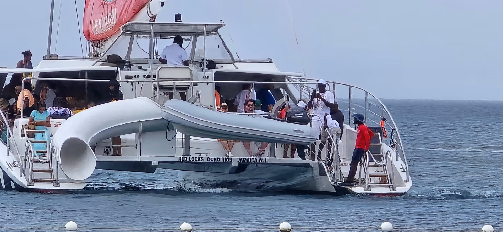 Large white catamaran with many people aboard on open sea.