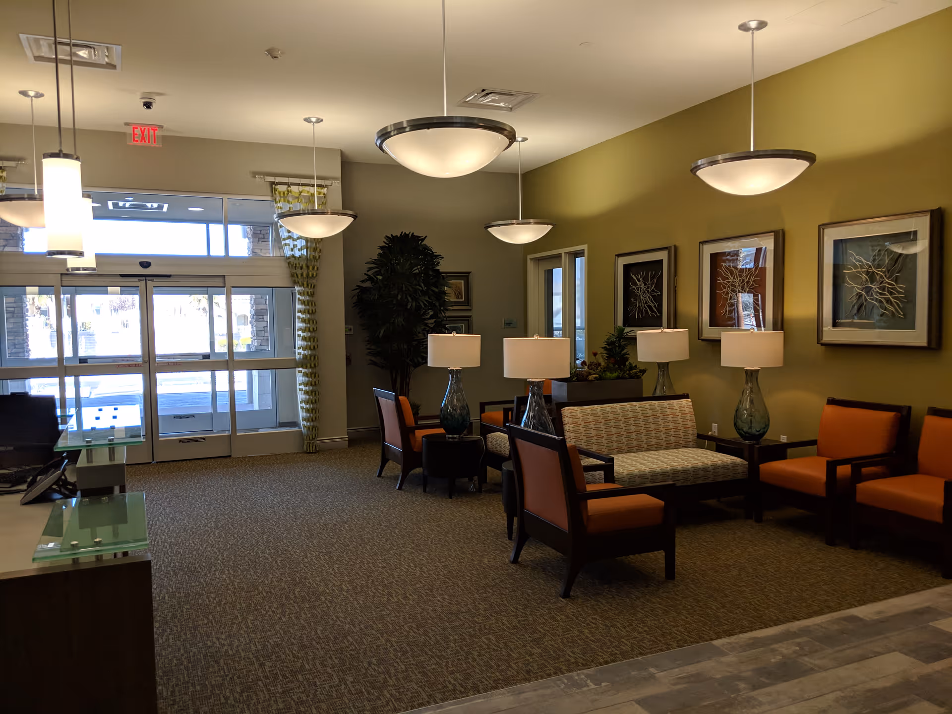 Senior living facility lobby with sofas, chairs, lamps, and wall art near glass doors.