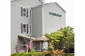 Front view of a multi-story gray senior living facility with a porch and landscaping.