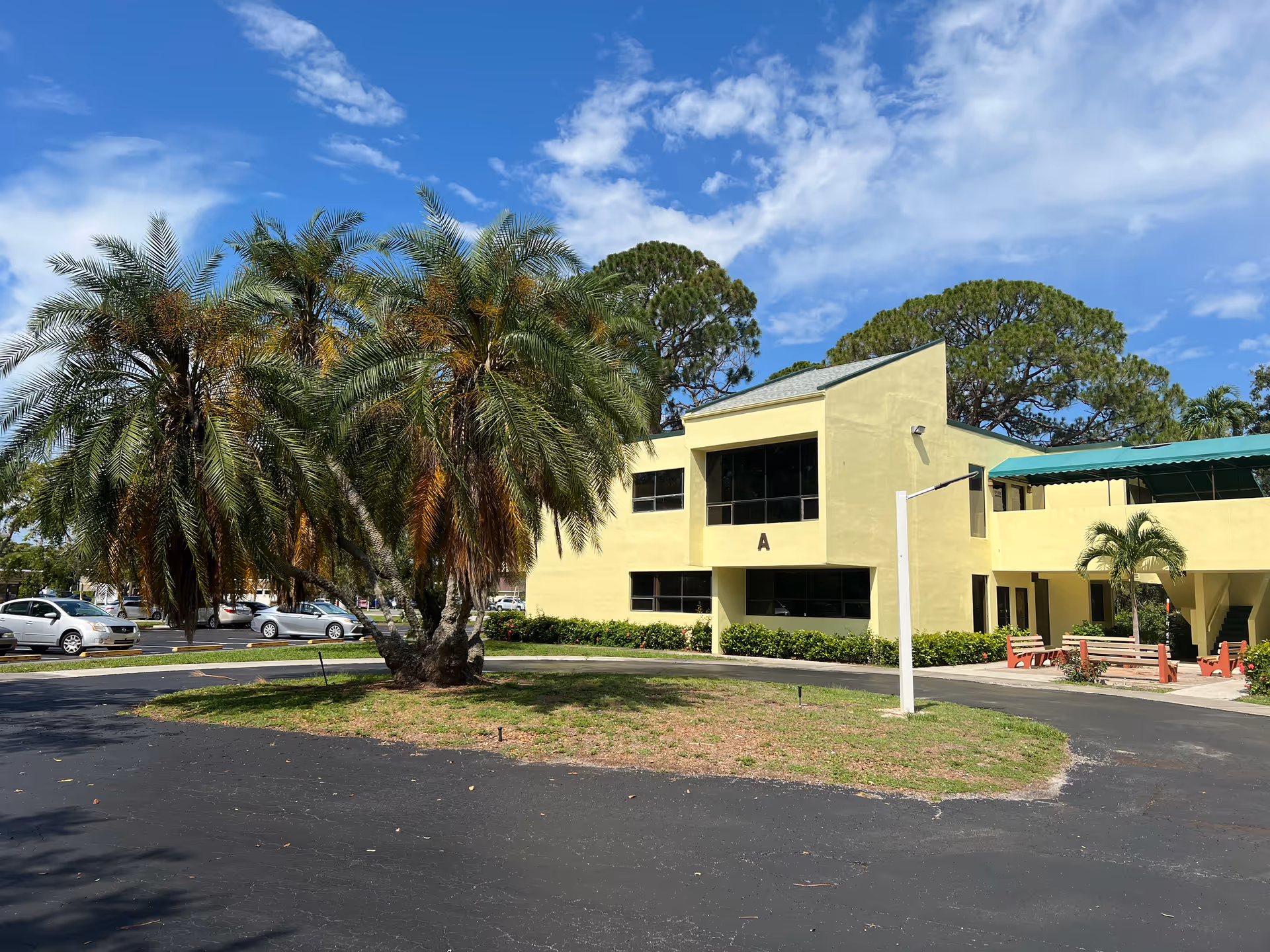 Exterior view of pale yellow two-story senior care facility with palm trees and a circular driveway.