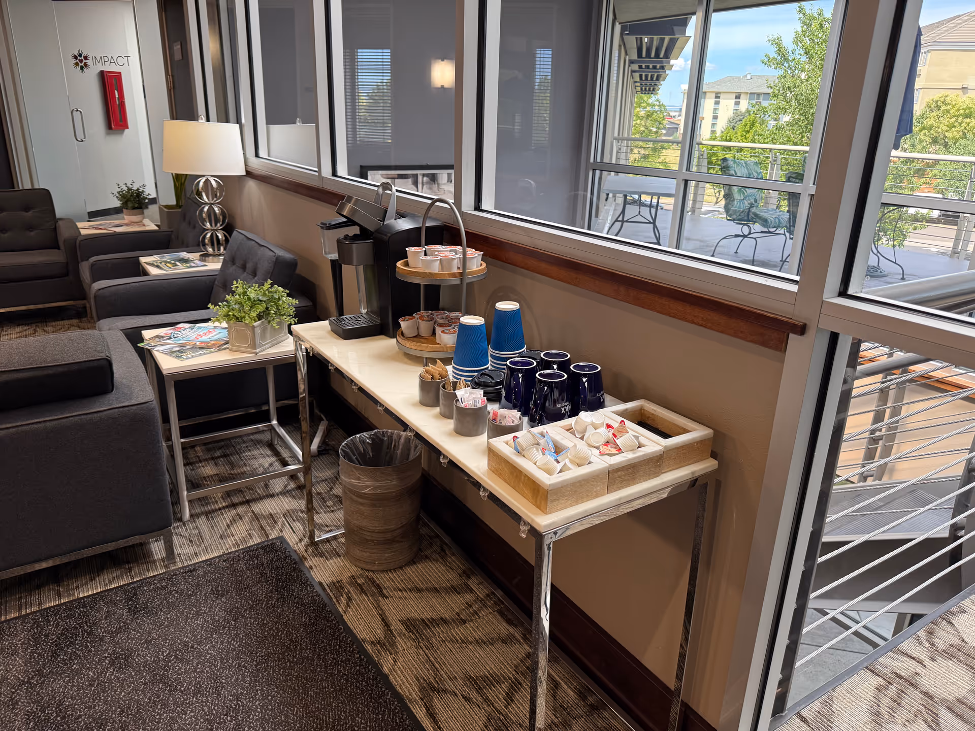 Interior lounge seating with a coffee station and large windows overlooking a balcony.