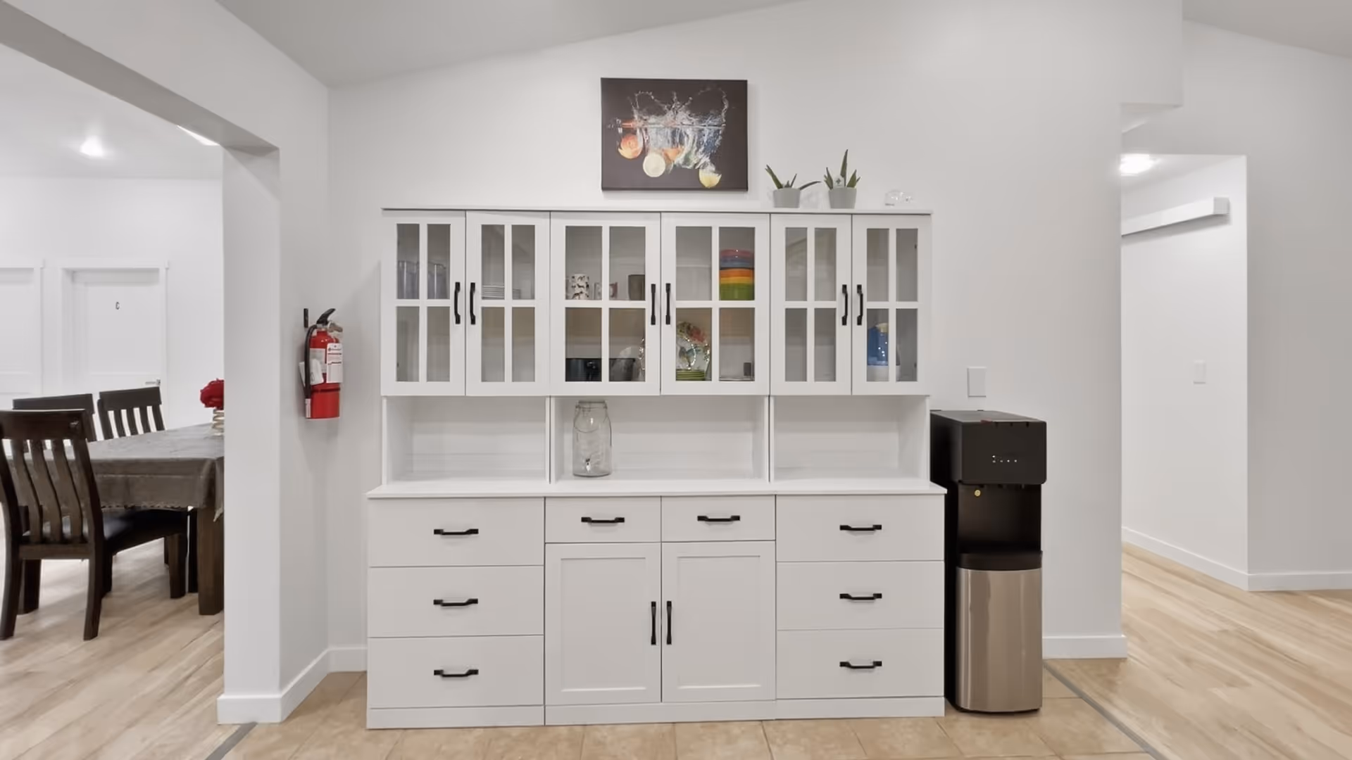 White cabinetry and coffee station in a bright dining area, with a table and chairs nearby