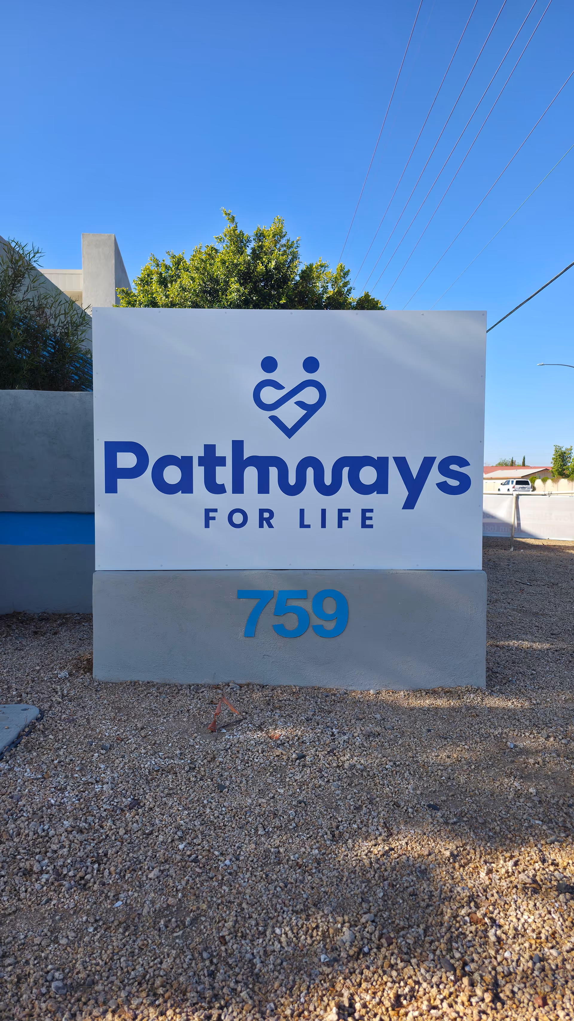 Large white Pathways For Life sign on a concrete base outdoors near a gravel lot.