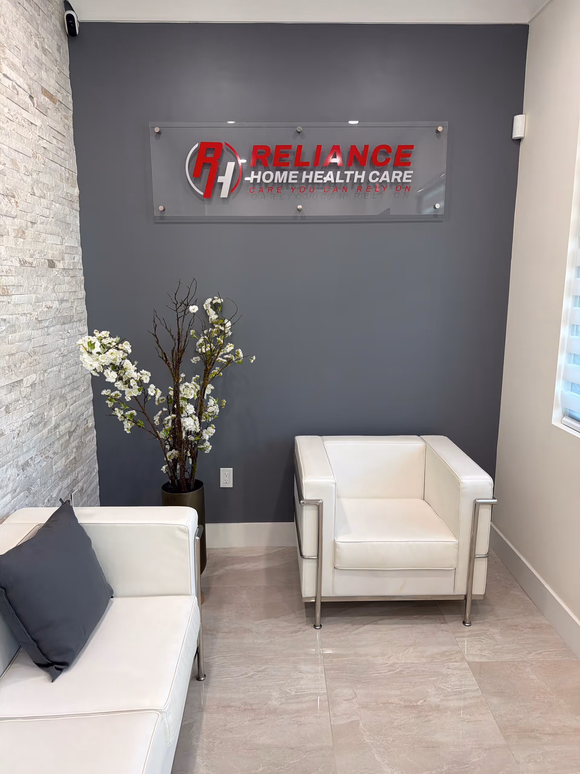 Modern waiting area with white armchairs, a gray wall, and a Reliance Home Health Care sign.