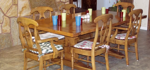 Rectangular wooden dining table surrounded by six wooden chairs with patterned seat cushions and colorful plastic cups on top.