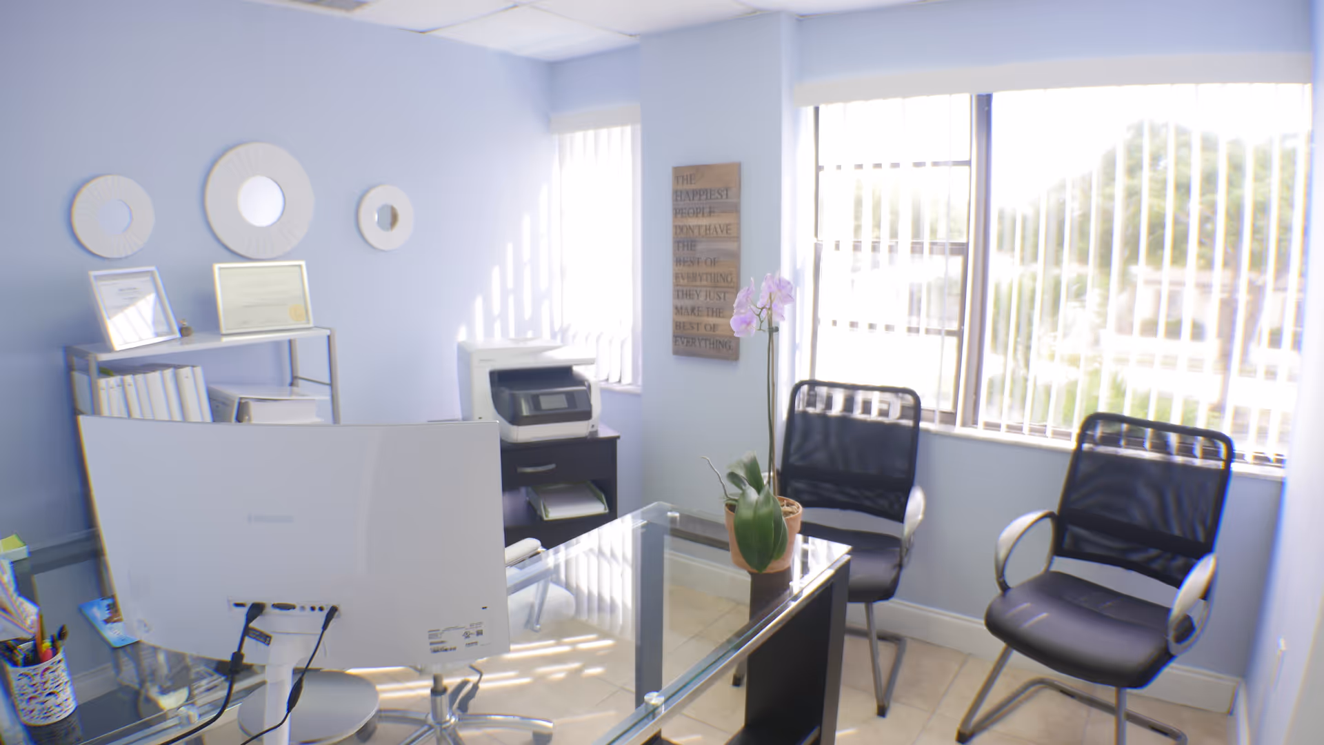 Blue-walled reception area with a glass desk, chair, printer, and potted orchid.