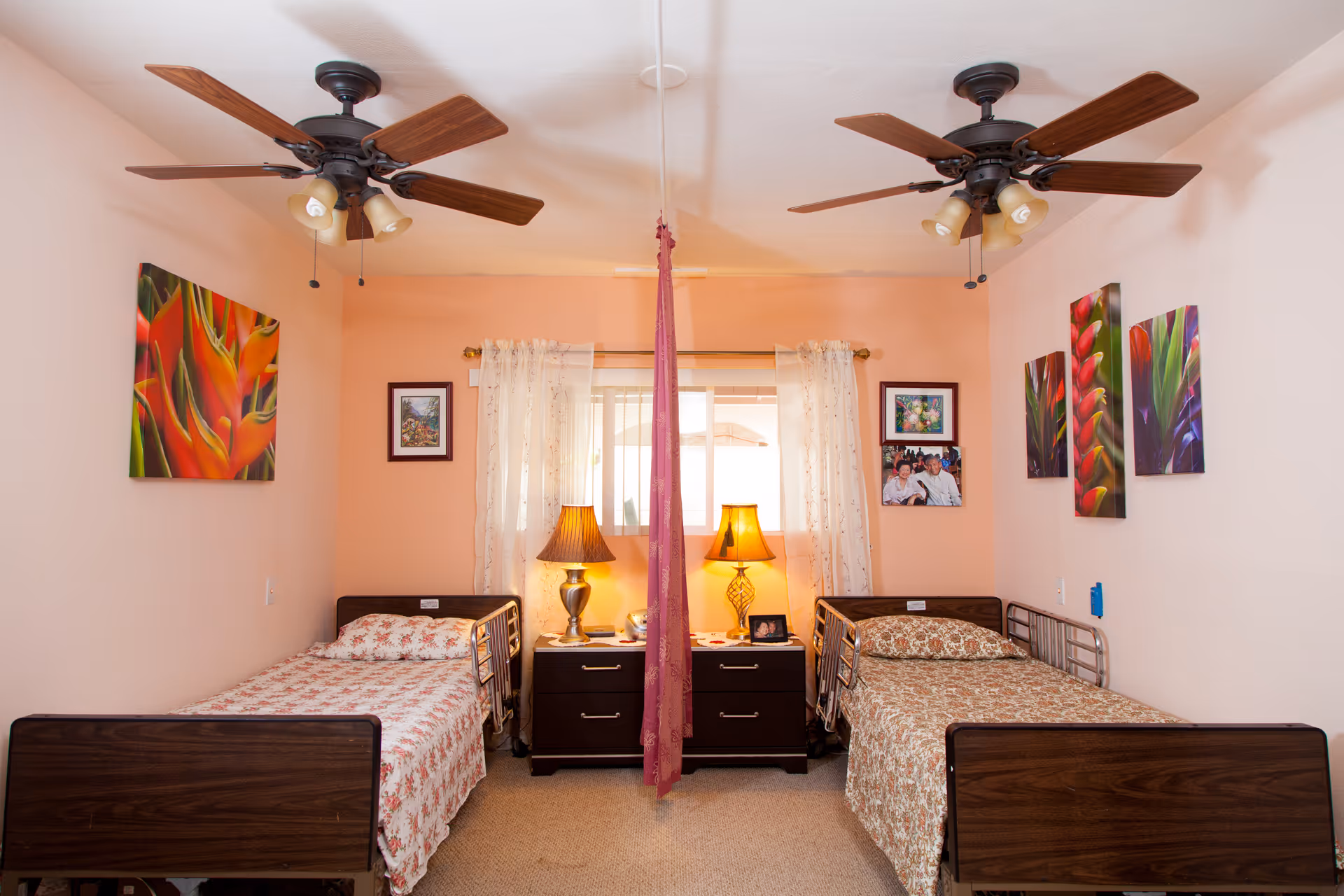 Two twin beds with nightstands and lamps flank a central window in a pink bedroom.