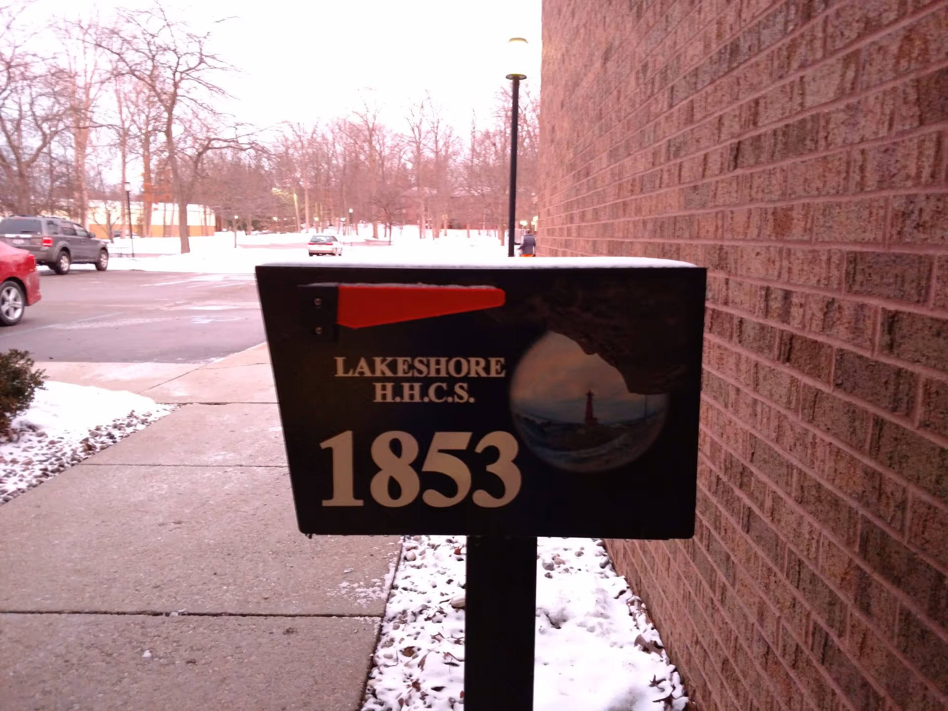 Lakeshore H.H.C.S. sign stands near a brick building along a snowy sidewalk.
