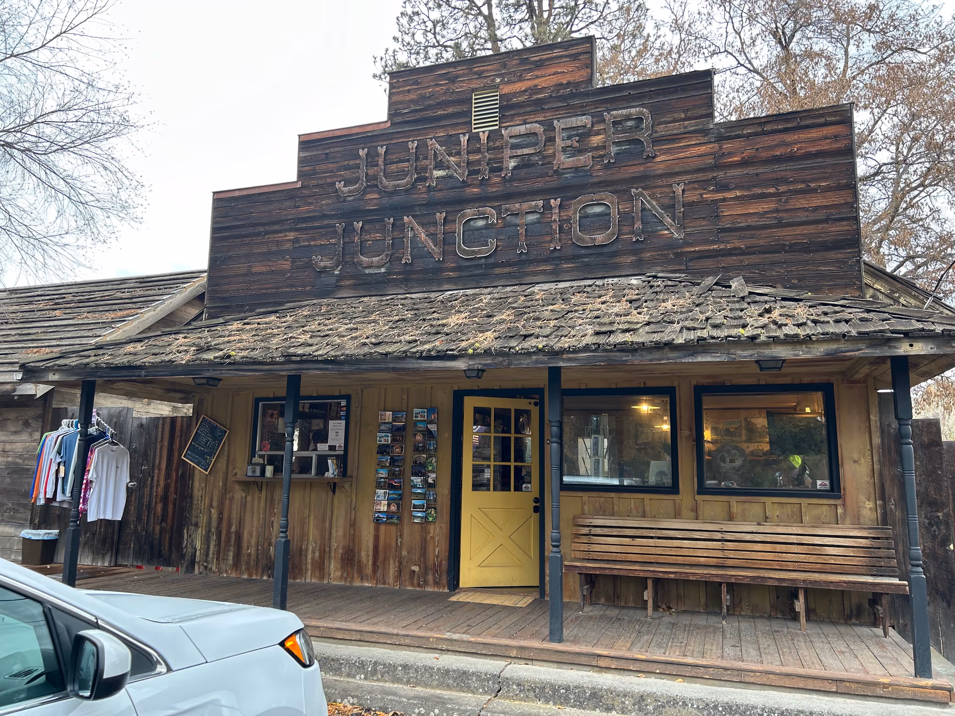 Rustic storefront with Juniper Junction sign, yellow door, and wooden bench on weathered porch