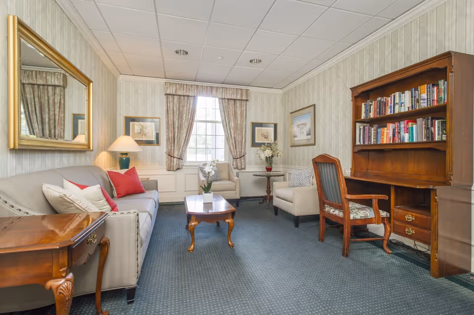 Cozy senior living lounge with sofa, chairs, coffee table, desk, and bookshelf.