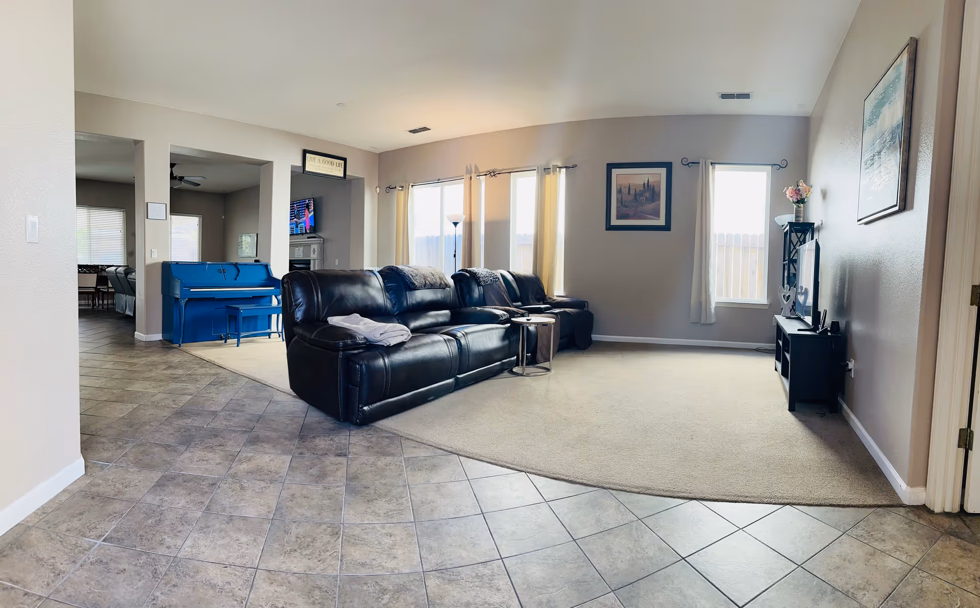 Spacious living room in a senior facility featuring a black leather sofa and large windows.