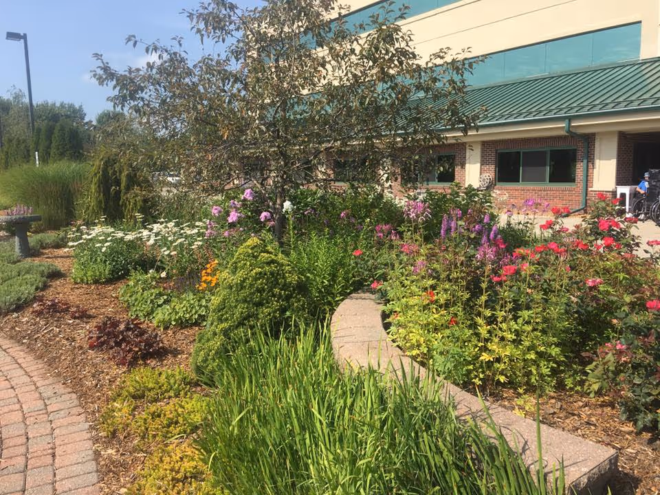 Well-kept flower beds and shrubs frame the brick senior living facility exterior.