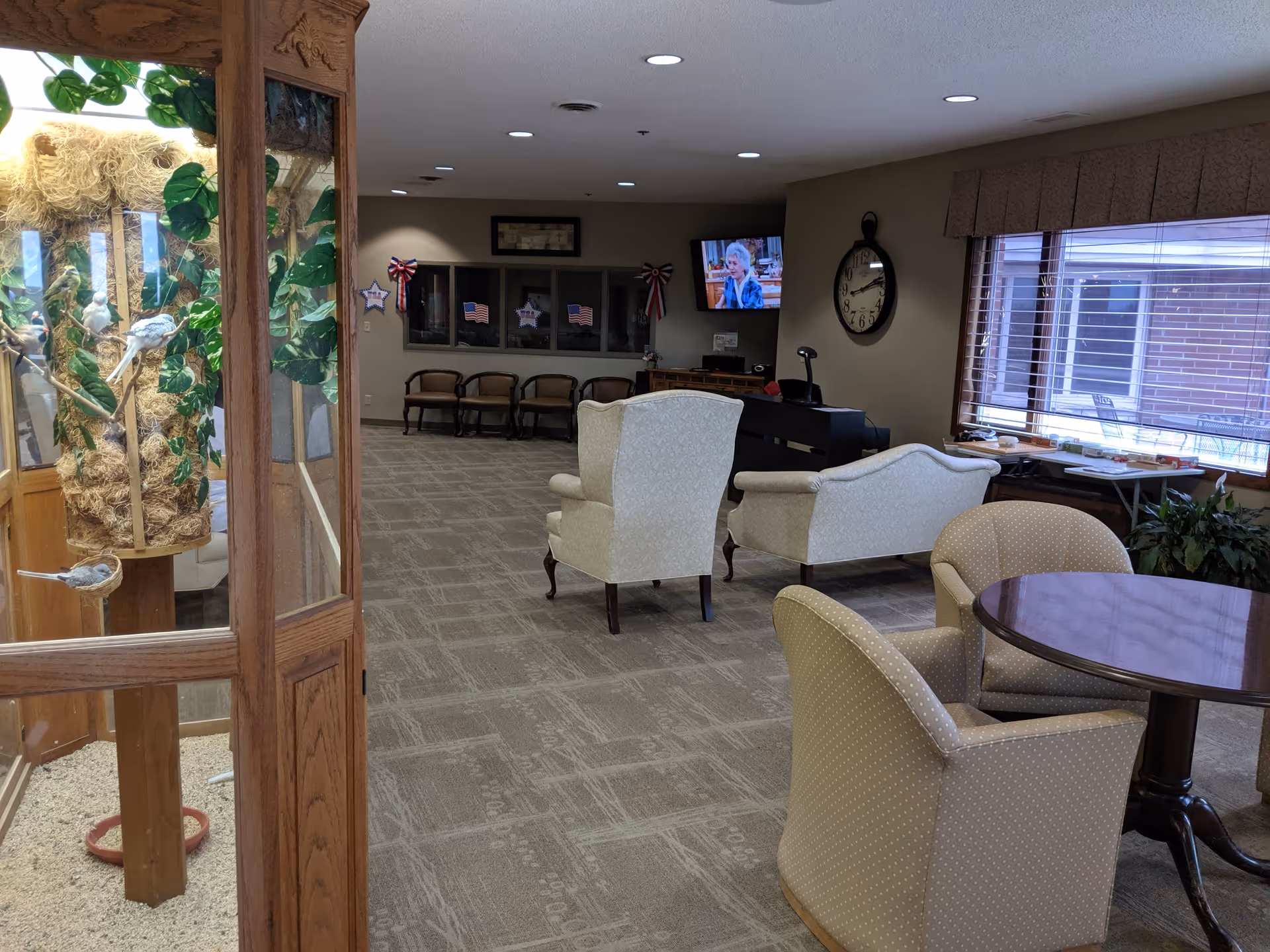 Interior senior living lounge with beige chairs, a round table, and TV.