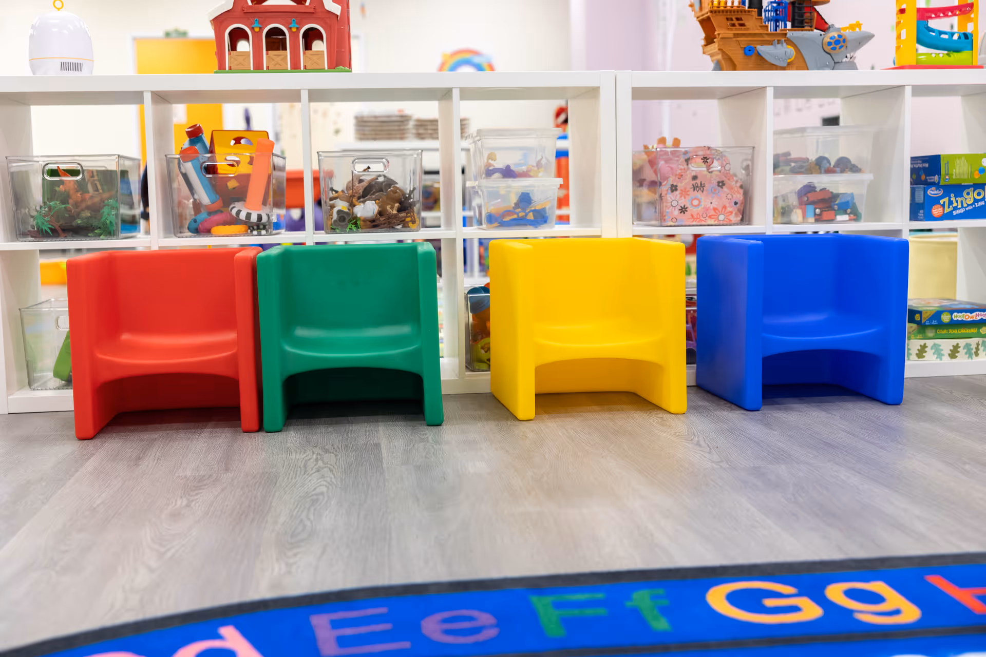 Colorful plastic children’s chairs line up in a bright playroom with toy shelves.