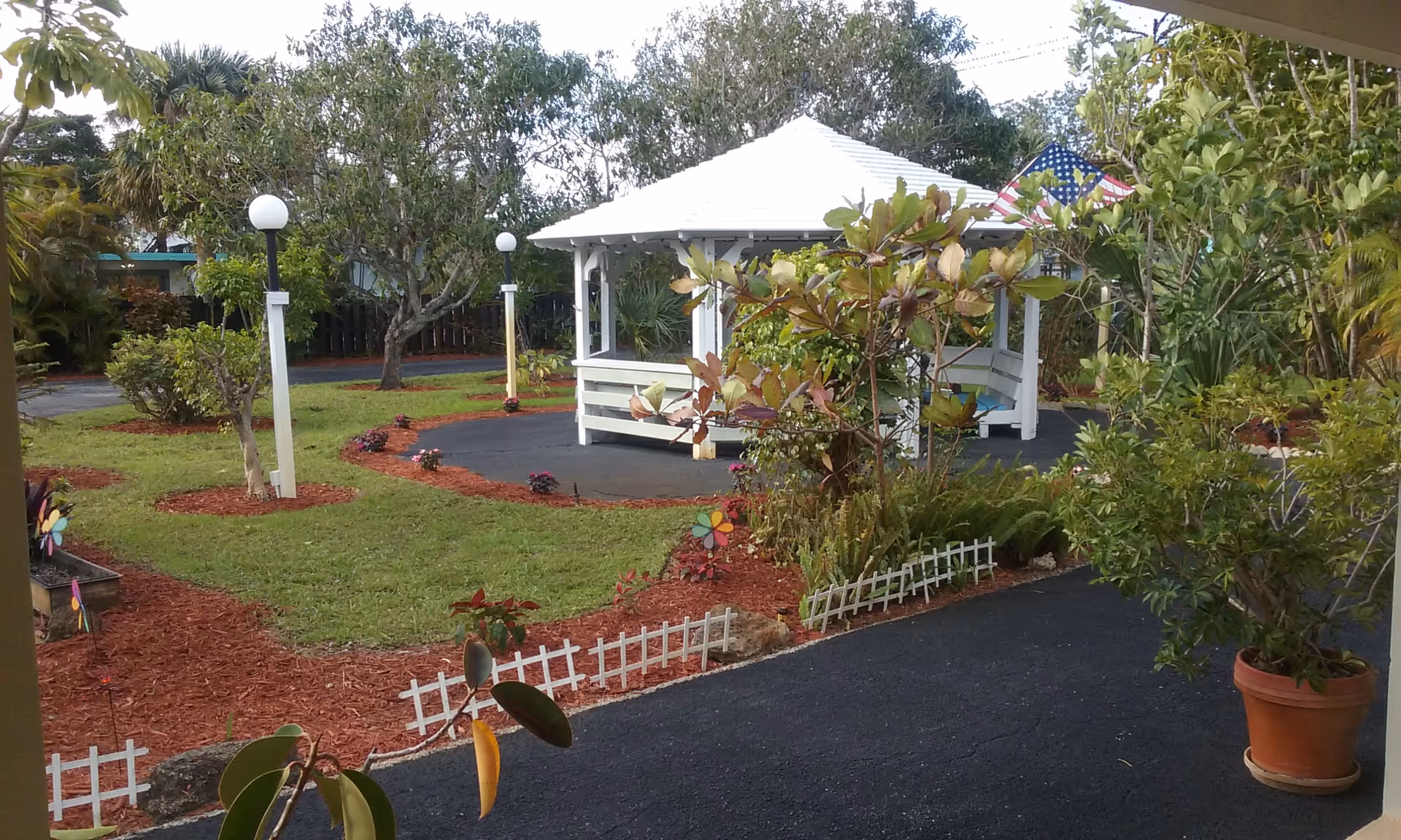 White gazebo surrounded by garden paths and plants in a sunny outdoor courtyard.